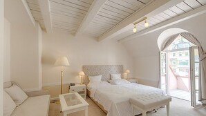 A bedroom with a bed, a nightstand, a bedside table, a bench, and a window with curtains. - Hotel Embassy (Karlovy Vary)