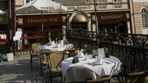 An outdoor seating area with tables and chairs, umbrellas, and signs for a hotel and a pub. - Hotel Embassy (Karlovy Vary)