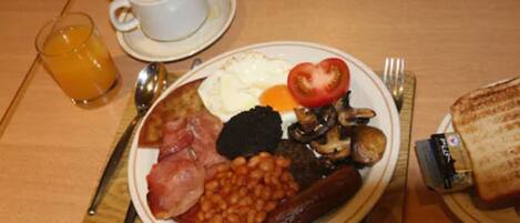 A breakfast plate with eggs, bacon, beans, mushrooms, and a sausage.