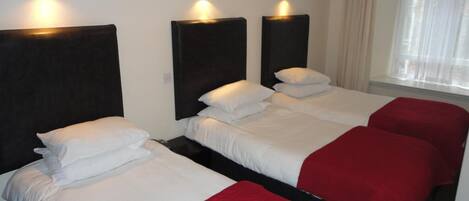 Habitación de hotel con dos camas, cada una con ropa de cama blanca y mantas rojas. Hay luces fijadas en la pared sobre cada cama.