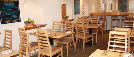 A restaurant with wooden tables and chairs, a blackboard with text, and a kitchen area in the background.