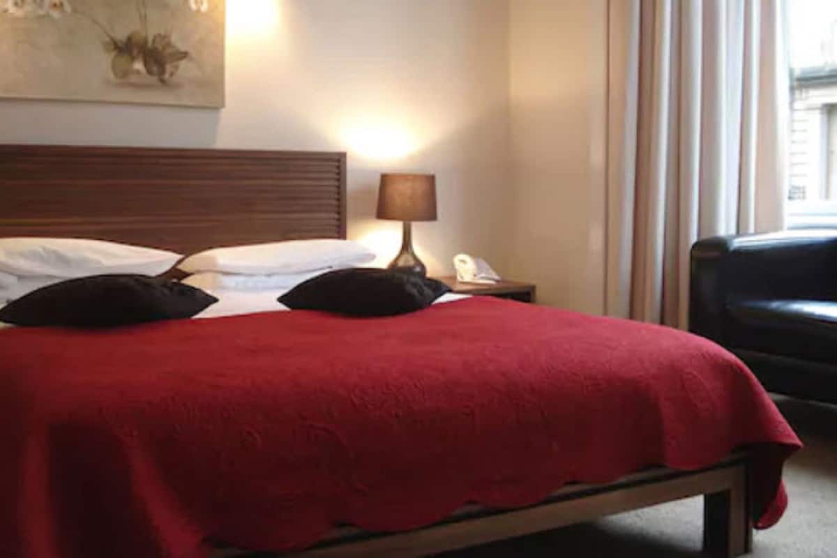 A hotel room with a bed, a nightstand with a lamp, and a chair.