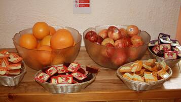 A buffet table with bowls of oranges and apples, and baskets of packaged food items.