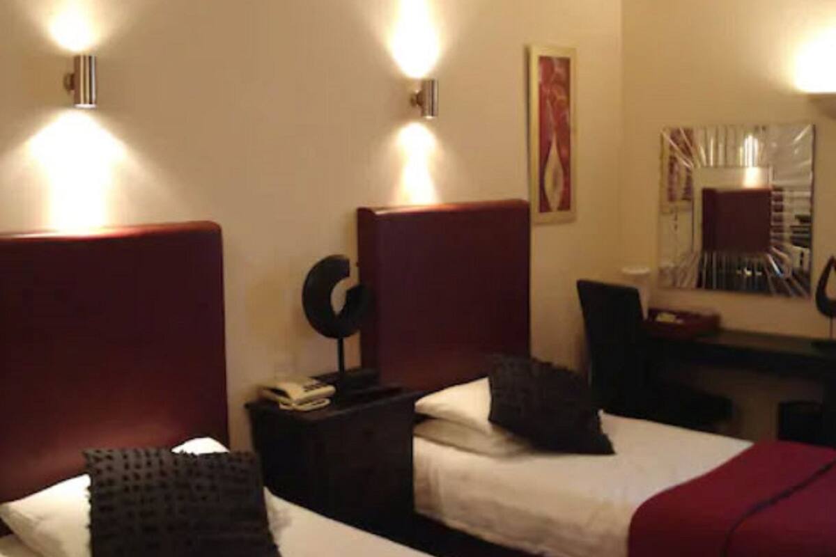 A hotel room with two single beds, a desk, a chair, and a mirror.