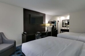 A hotel room with two beds, a desk with a flat-screen TV, a chair, a lamp, and a mirror.