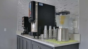 Een commerciële koffiemachine met een melkopschuimer en een grote kan, waarschijnlijk bedoeld voor het maken van lattes of cappuccino's, op een aanrecht met een betegelde spatwand.