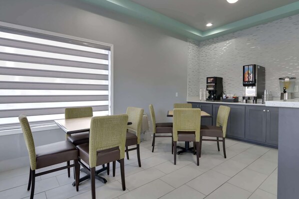A dining area with a table and chairs, a kitchen counter with appliances, and a window with blinds.