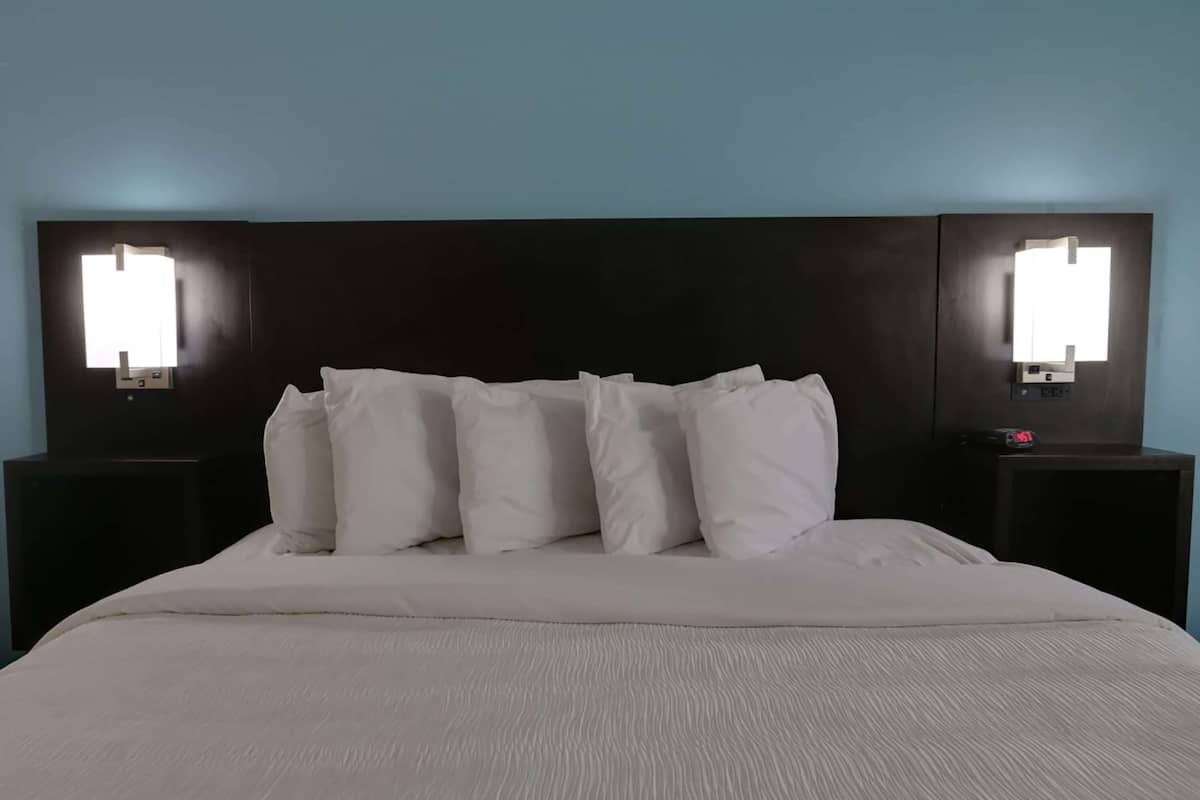 Una habitación de hotel con una cama grande, ropa de cama blanca y dos mesitas de noche con lámparas fijadas a la pared.
