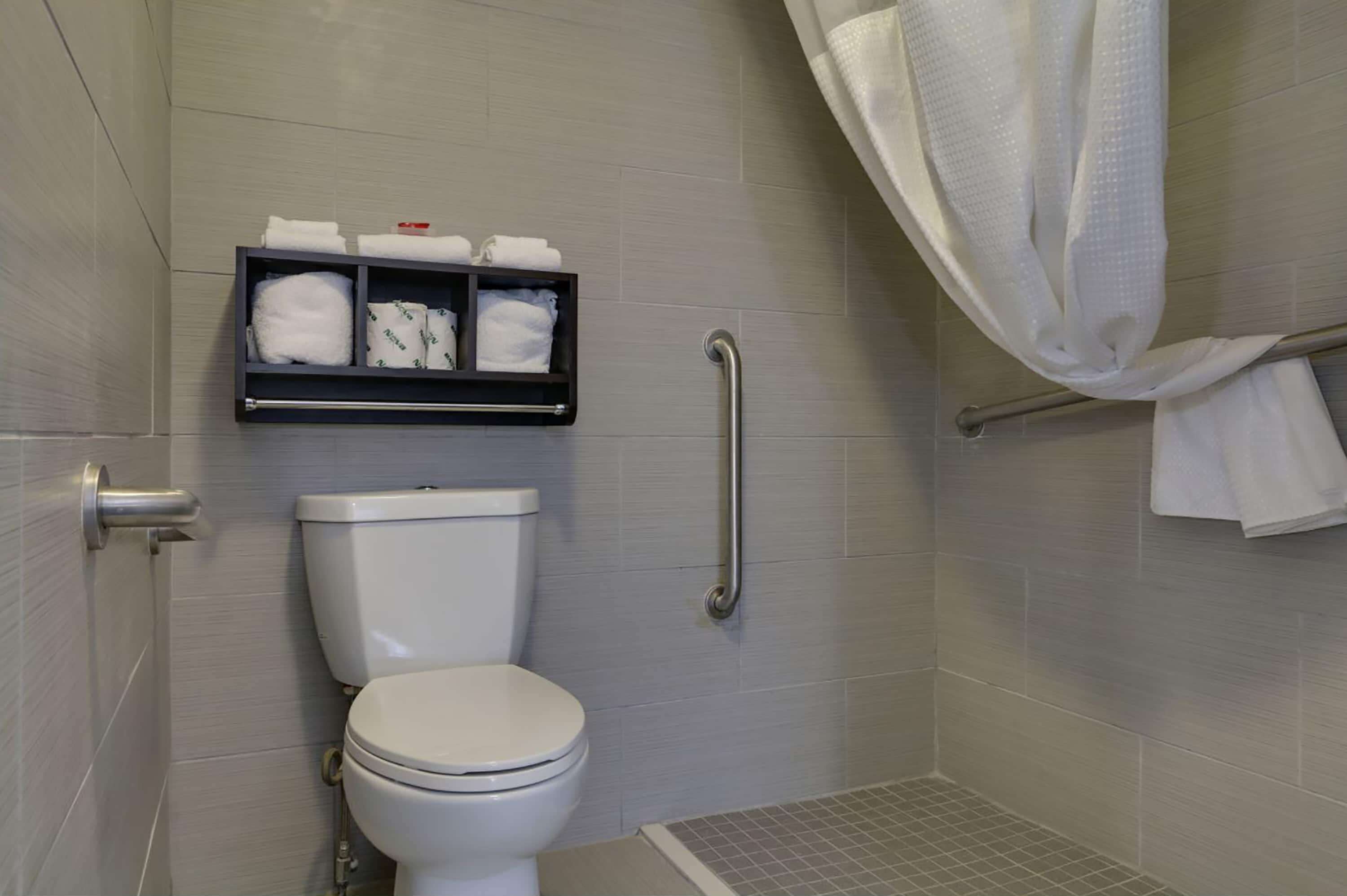 A bathroom with a toilet, a shelf with towels, a shower curtain, and a grab bar.