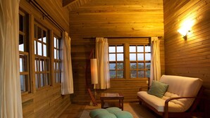 Ein gemütliches Blockhäuschen mit Holzwänden, einer Couch, einem passenden Hocker und einem Fenster mit Vorhängen.