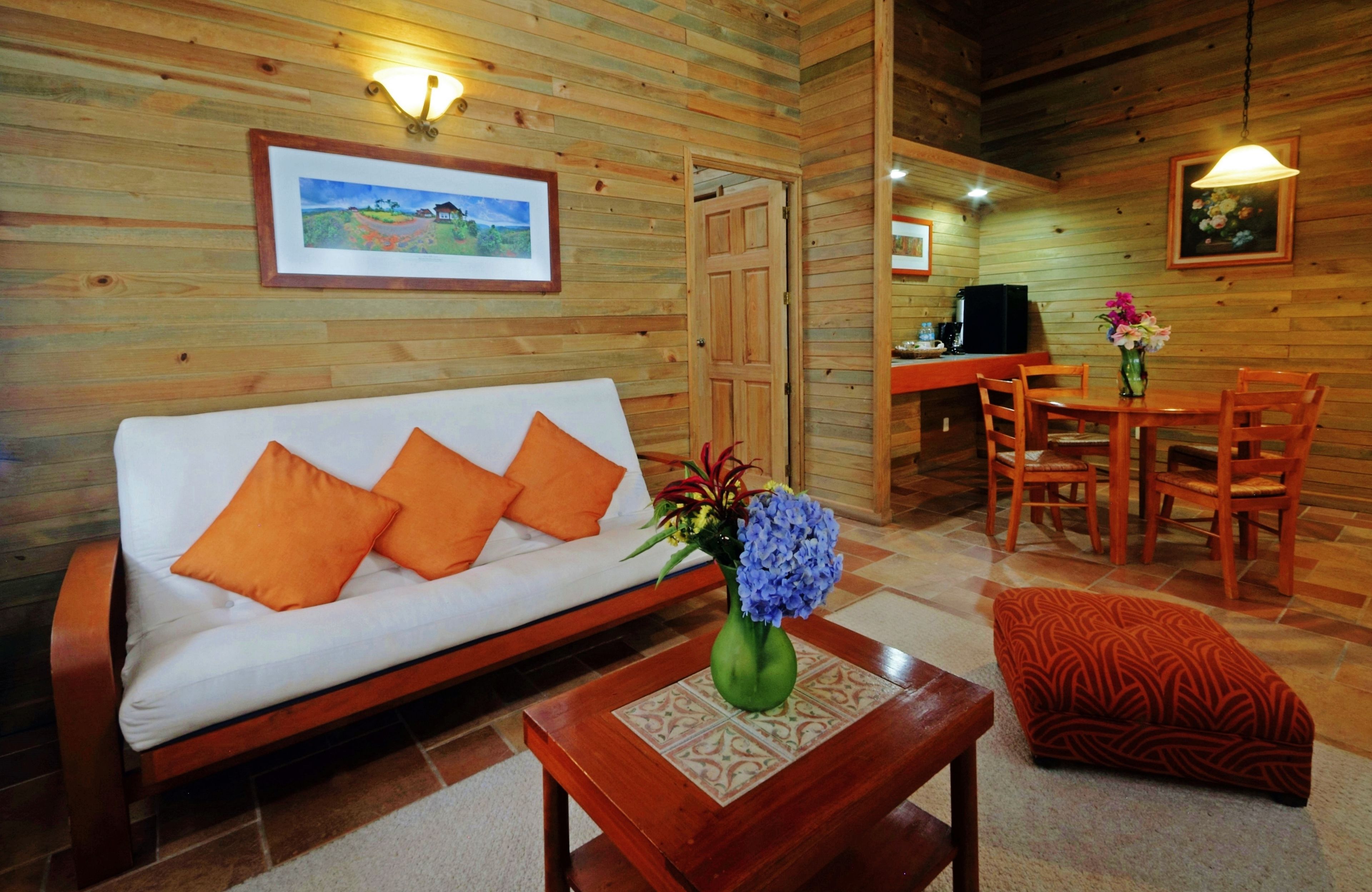 A wooden interior with a sofa, a dining table with chairs, and a small kitchen area.
