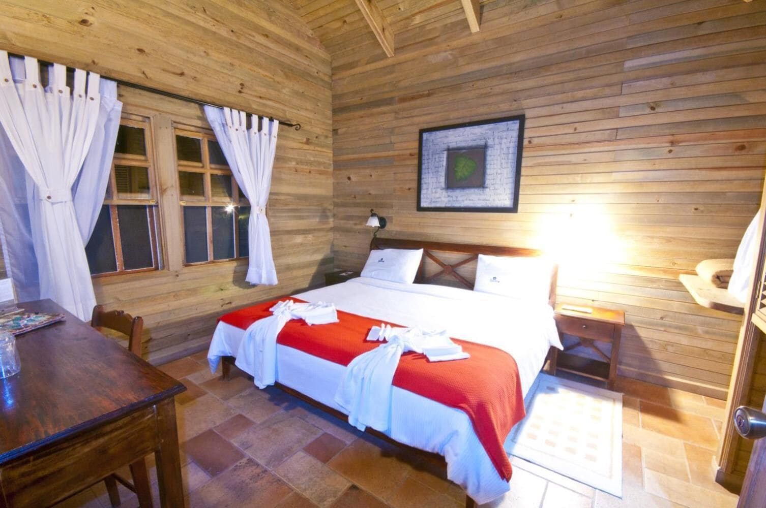 Una camera in legno con un letto, un tavolo e una finestra con tende.