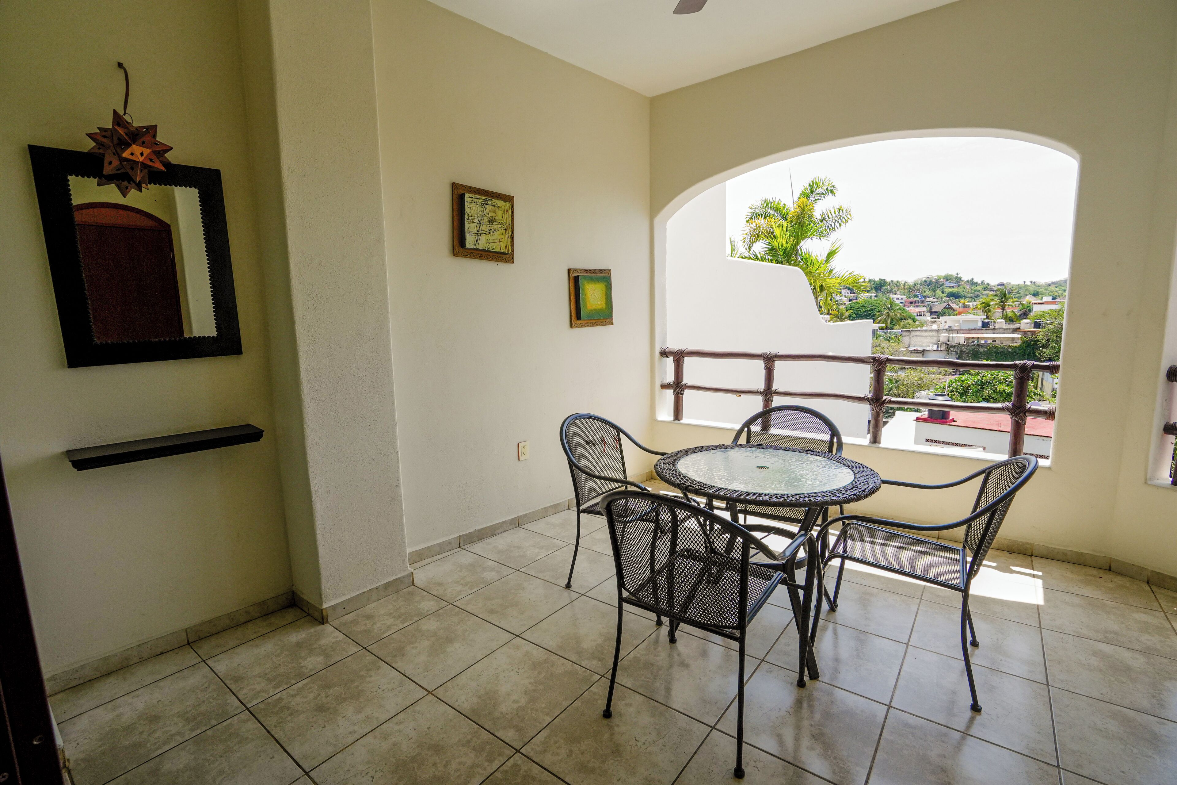 A balcony with a round table and chairs, a small shelf, and a framed picture on the wall.