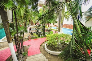 Un espace piscine avec un chemin rouge, des palmiers et un bâtiment doté d’un toit de chaume.