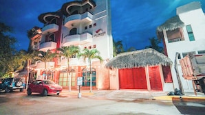 A hotel with a modern design, featuring a multi-story structure with balconies, a thatched-roof building, and a red car parked in front. - Hotel y Suites Los Encantos (Sayulita)