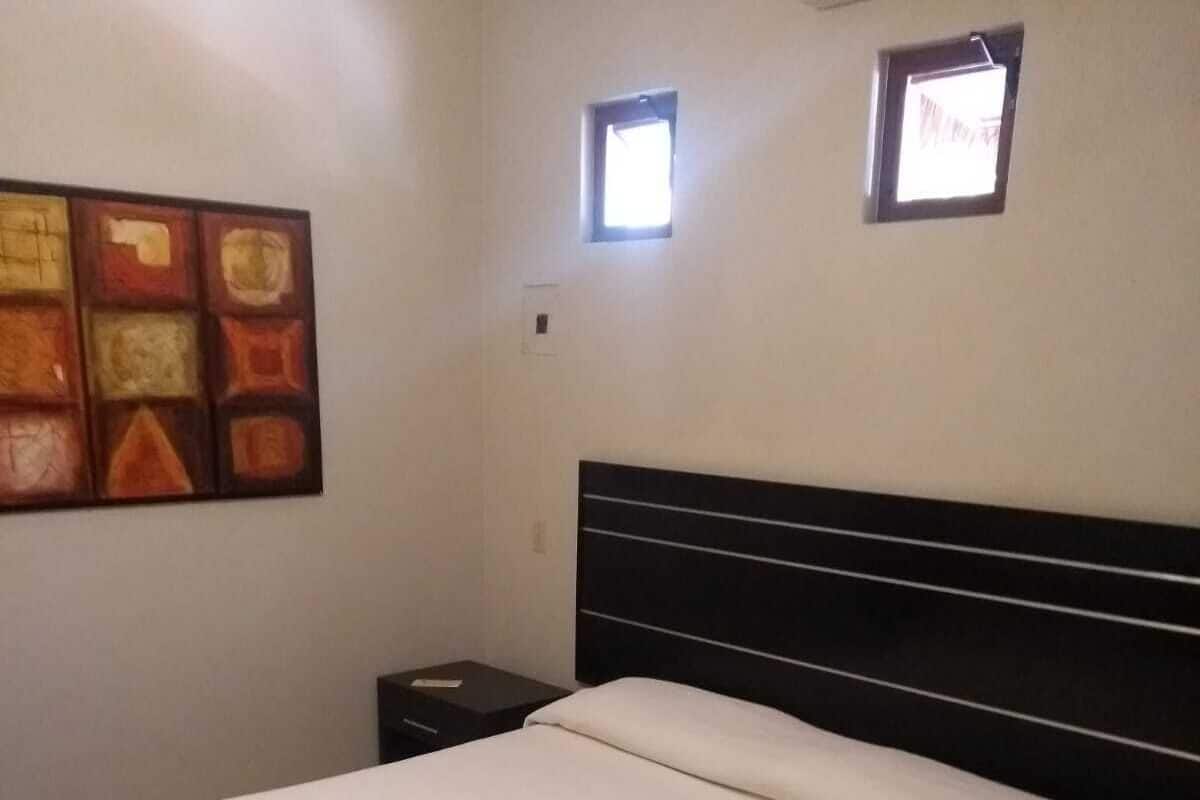Habitación de hotel con cama, mesita de noche, aire acondicionado de pared y una ventana pequeña.