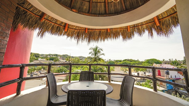 A balcony with wicker furniture, a thatched roof, and a view of a cityscape. - Hotel y Suites Los Encantos (Sayulita)