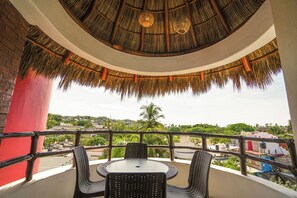 A balcony with wicker furniture, a thatched roof, and a view of a cityscape. - Hotel y Suites Los Encantos (Sayulita)
