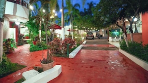 A red-tiled pathway leading to a building with a balcony, surrounded by potted plants and palm trees. - Hotel y Suites Los Encantos (Sayulita)