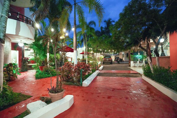 A red-tiled pathway leading to a building with a balcony, surrounded by potted plants and palm trees. - Hotel y Suites Los Encantos (Sayulita)