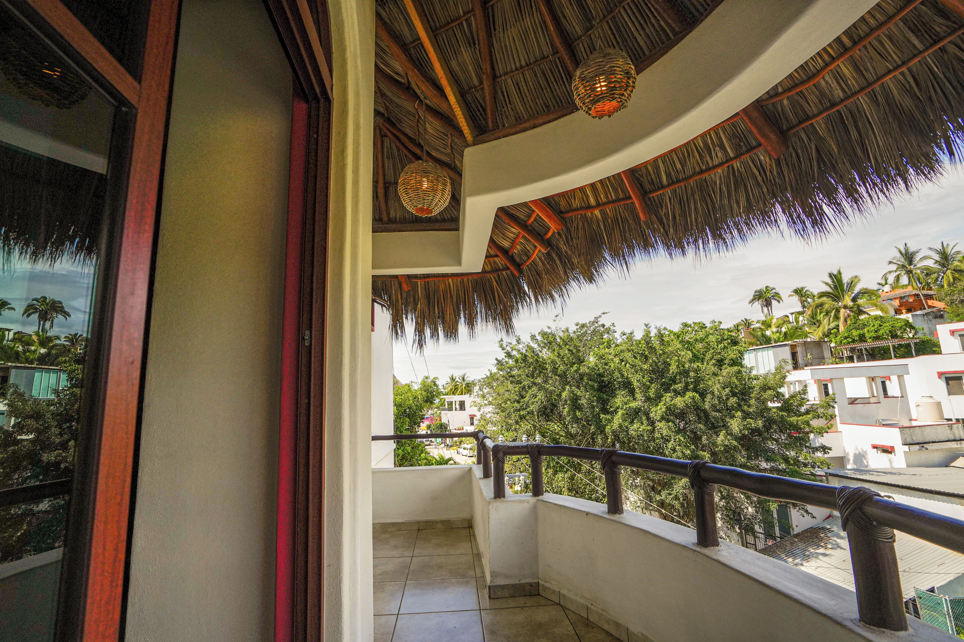 A balcony with a thatched roof, a view of the surrounding buildings, and a railing.