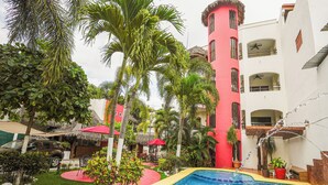 A swimming pool surrounded by palm trees and a building with a red tower. - Hotel y Suites Los Encantos (Sayulita)