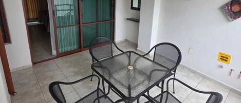 A room with a glass-top table and four chairs, a ceiling fan, a sliding glass door, and a small shelf with items.
