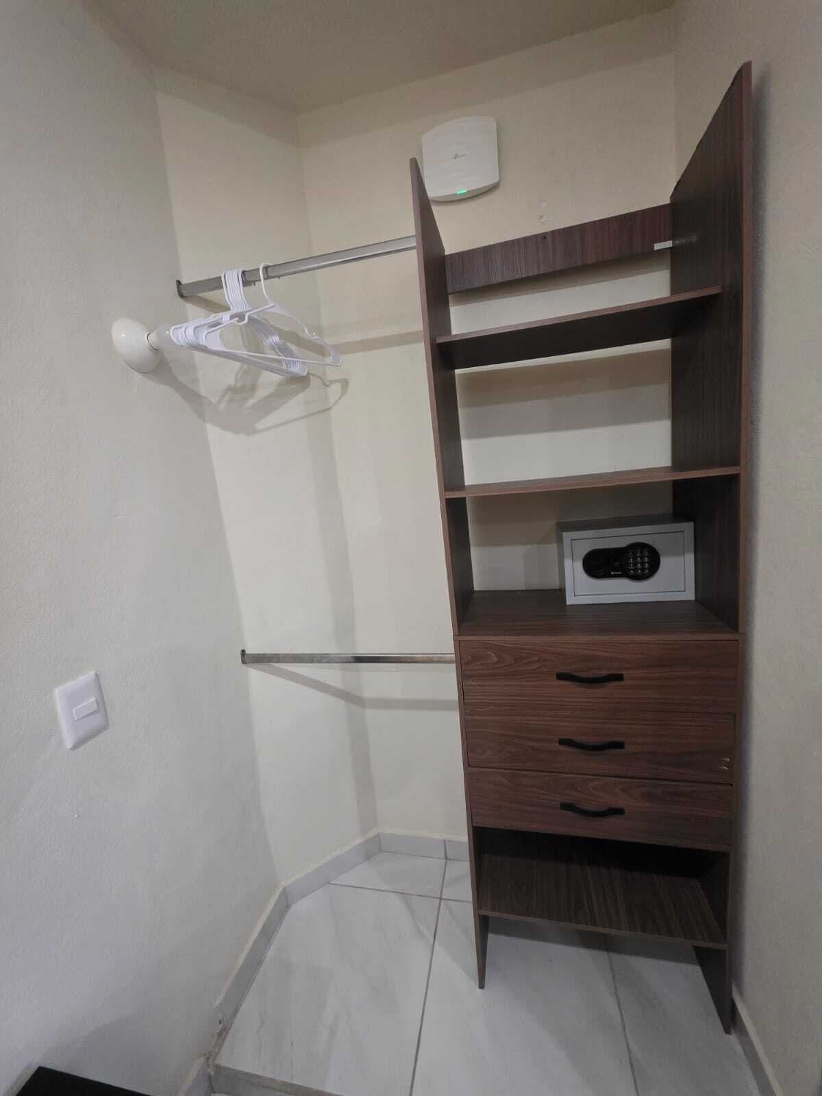 Habitación de esquina con un armario de madera, un perchero blanco y un termostato en la pared.