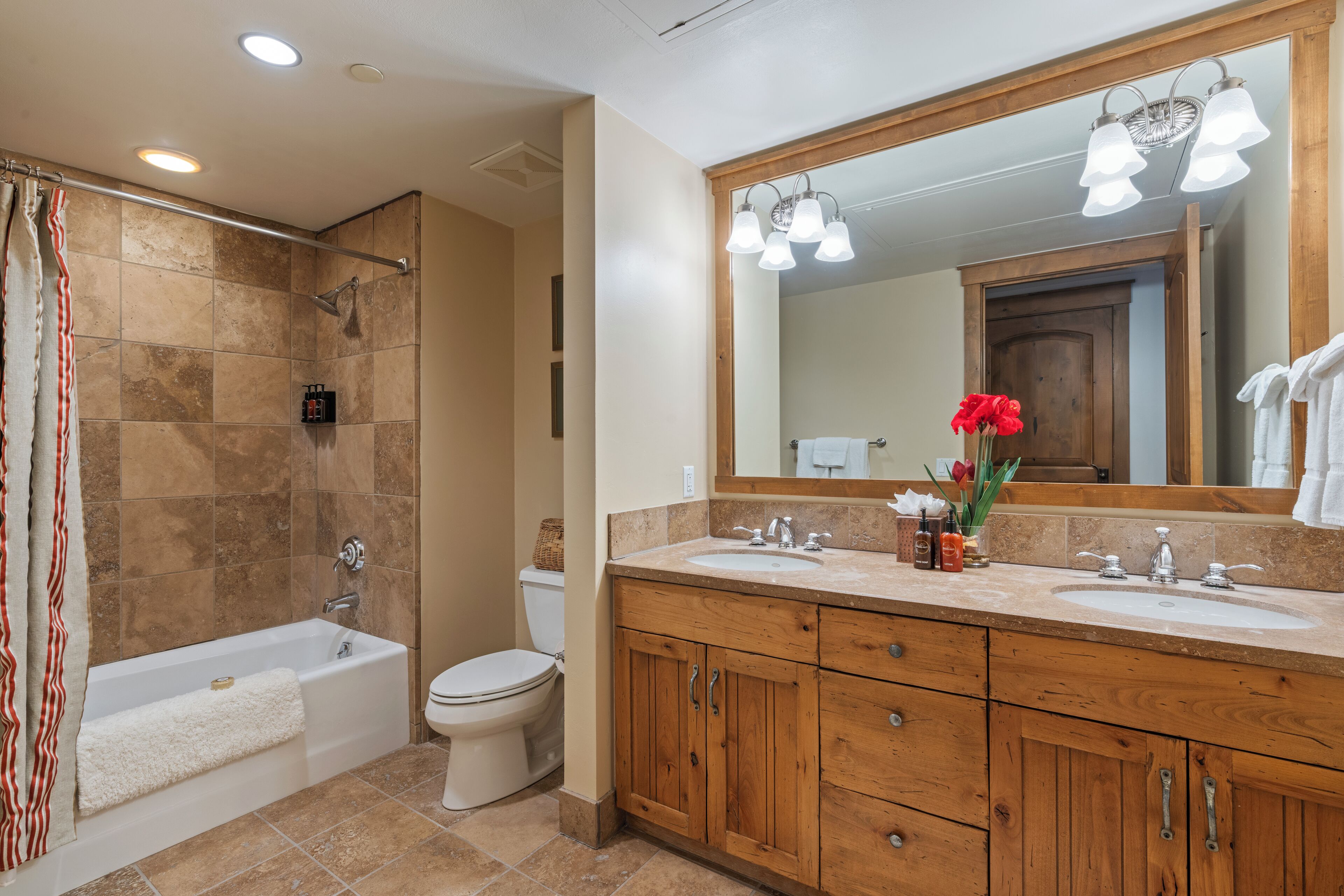 A bathroom with a bathtub, toilet, wooden vanity, and a large mirror.