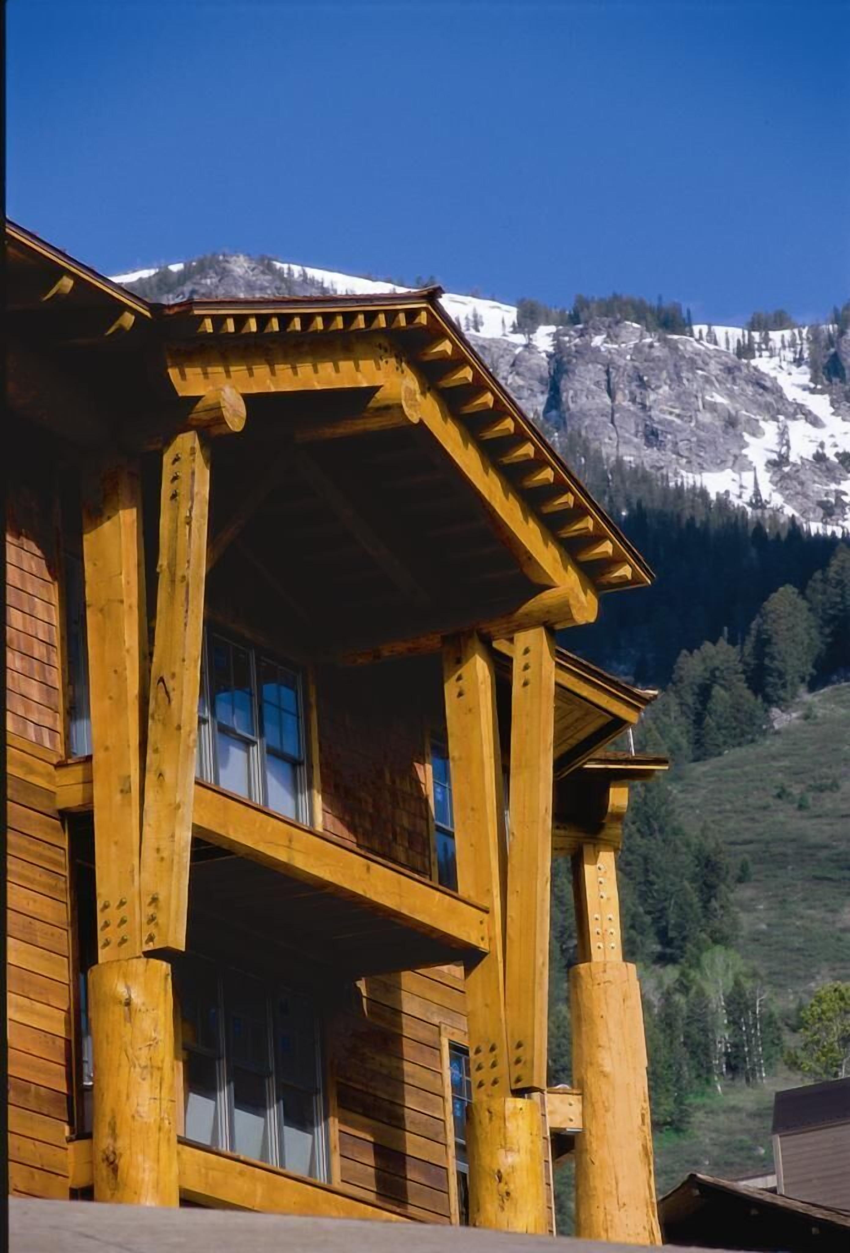 A wooden chalet with a balcony, set against a mountainous backdrop.