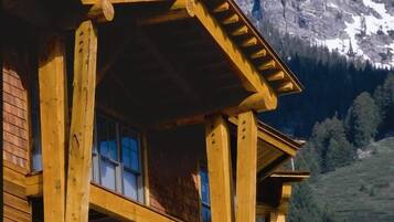 A wooden chalet with a balcony, set against a mountainous backdrop.