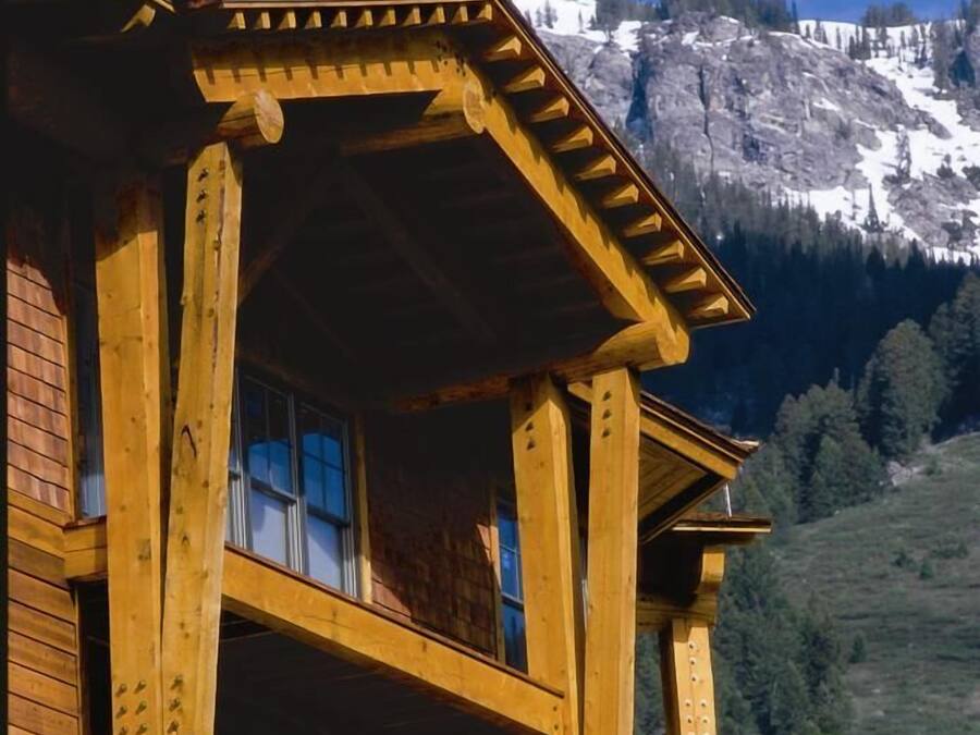 A wooden chalet with a balcony, set against a mountainous backdrop.