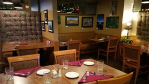 A restaurant interior with wooden tables and chairs, framed pictures on the walls, and a patterned wall. - Soldotna Inn (Soldotna)