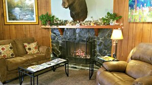 A cozy living room with a stone fireplace, a mounted moose head, a framed landscape painting, and a colorful garden scene painting. - Soldotna Inn (Soldotna)