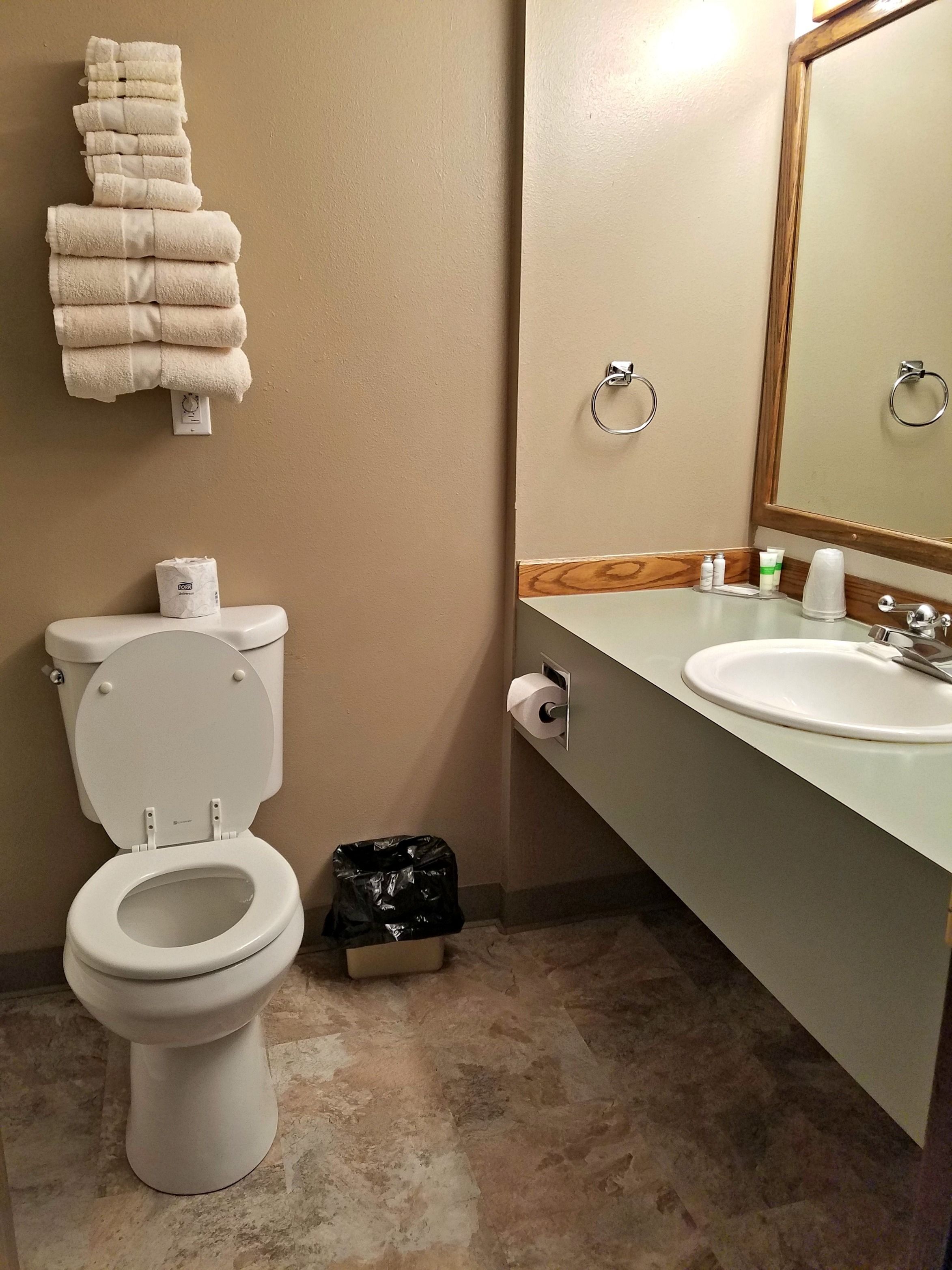 A bathroom with a toilet, a sink, a mirror, and a stack of towels.