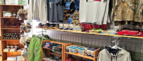 A clothing store with racks of t-shirts, hoodies, and other apparel, shelves with hats and mugs, and a display of folded clothes.