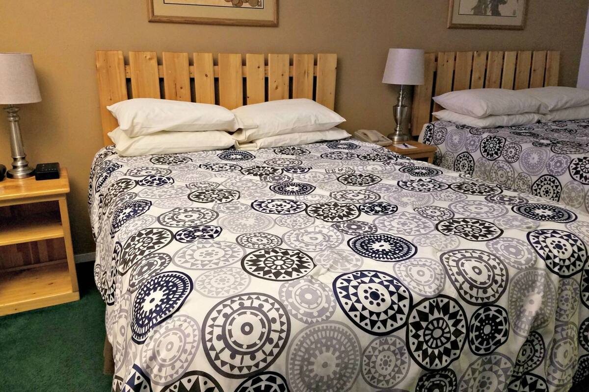 A hotel room with two beds, each with patterned bedding, wooden headboards, bedside lamps, and a small wooden nightstand with a lamp.