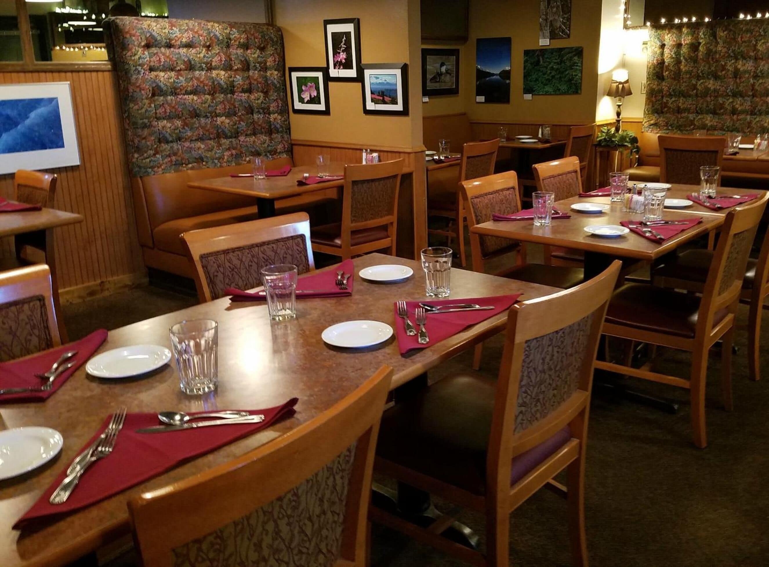 A restaurant with wooden tables and chairs, each set with plates, cutlery, and glasses.
