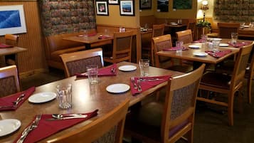 Un restaurante con mesas y sillas de madera, cada conjunto con platos, cubiertos y vasos.