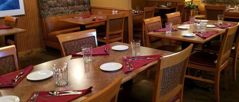 Ein Restaurant mit Holztischen und -stühlen, an jedem Tisch Geschirr, Besteck und Gläser.