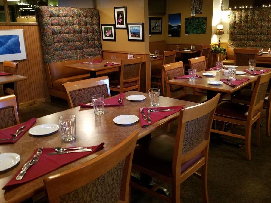 Un restaurante con mesas y sillas de madera, cada conjunto con platos, cubiertos y vasos.