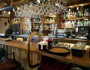 A bar area with a wooden counter, a cash register, and a variety of liquor bottles.
