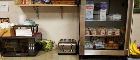 A kitchen counter with a microwave, toaster, and refrigerator stocked with various food items.