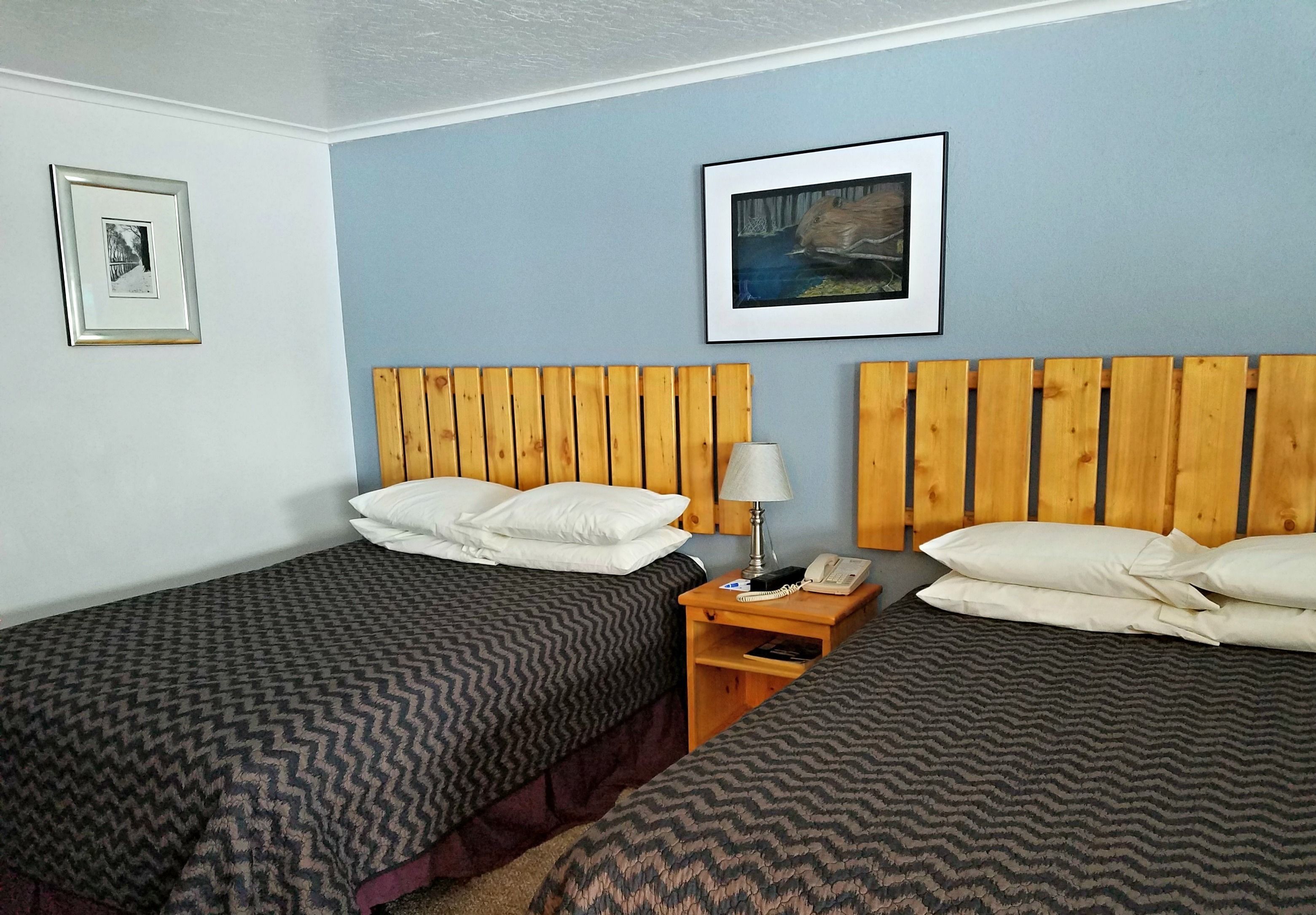 Une chambre avec deux lits, chacun doté d’une tête de lit en bois, d’une table de chevet avec une lampe et de tableaux encadrés accrochés au mur.