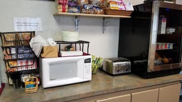 A kitchen counter with a microwave, toaster, and various food items. A sign indicates hot water is located on the coffee maker.