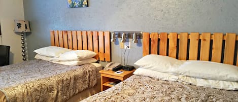 A hotel room with two beds, a wooden headboard, a bedside table with a phone and lamp, and two floral wall art pieces.