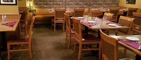 Un restaurante con mesas y sillas de madera, papel tapiz floral y luces colgantes en el techo.