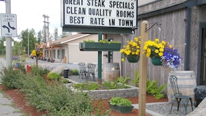 A restaurant with outdoor seating, a sign advertising steak specials and clean rooms, and a directional sign for the center lane. - Soldotna Inn (Soldotna)