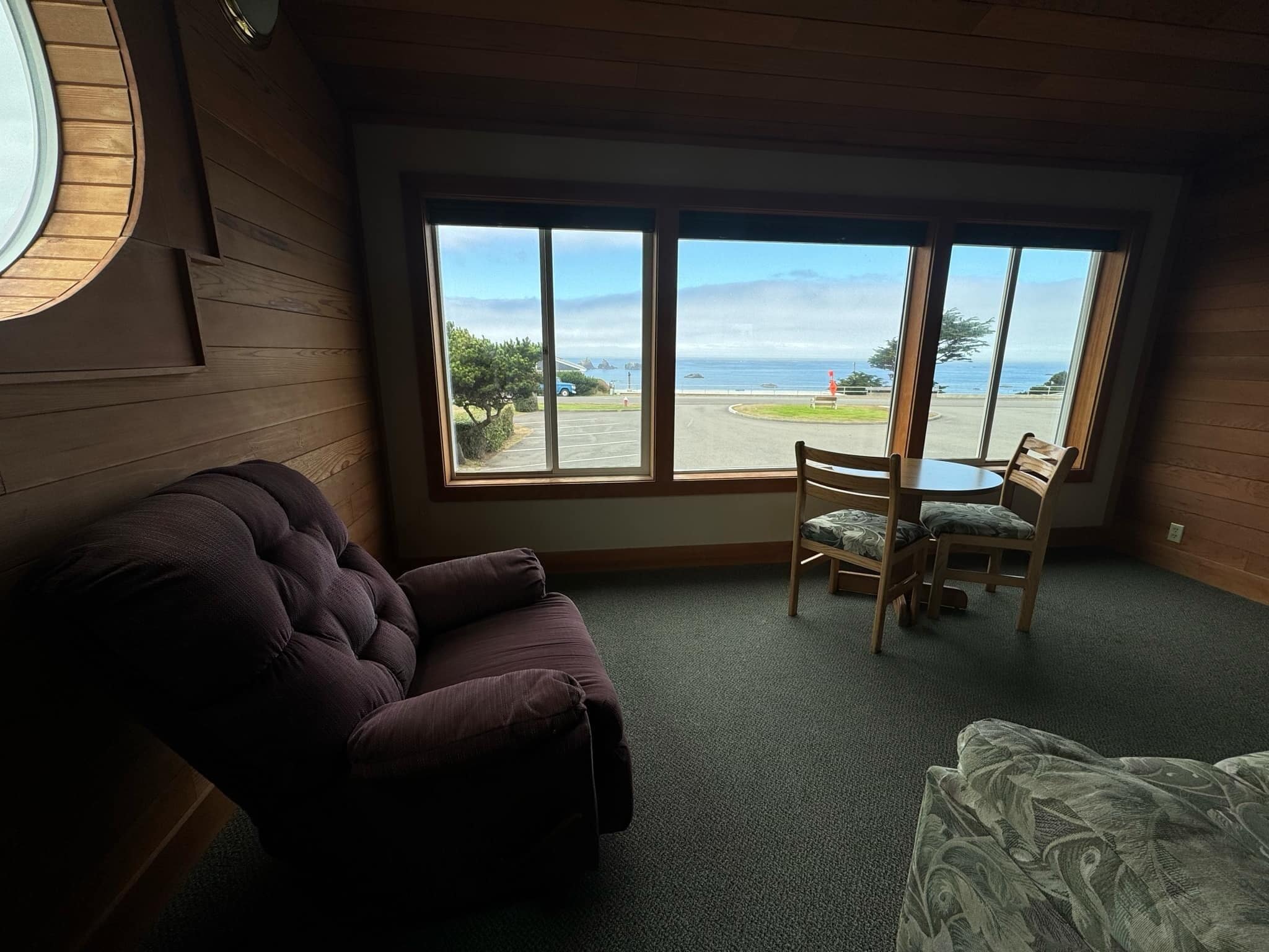 Una habitación con un ventanal grande, techo de madera, un sillón morado y una pequeña mesa con dos sillas.