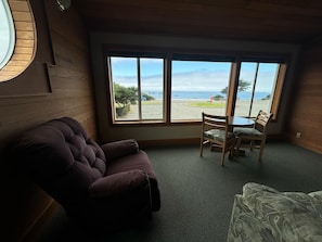 A room with a large window, a wooden ceiling, a purple armchair, and a small table with two chairs.